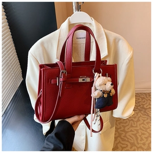 Detail of burgundy lychee leather handbag with classic metal lock and teddy bear charm