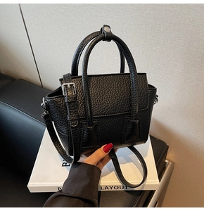 Detail of black lychee grain leather mini tote with silver hardware on white books