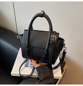 Close-up of black lychee grain leather handbag with dual handles and magnetic flap closure