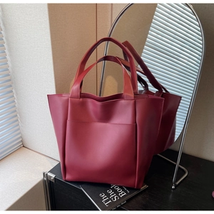 Detail view of burgundy leather tote bag with wide handle and front pocket against a mirror