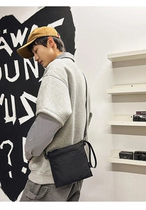 Street style shot of a black minimalist envelope crossbody bag worn by a male model