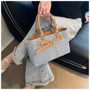Close-up of blue denim tote bag with brown leather handles and gold metal accents