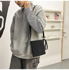 Detail of a black nylon envelope crossbody bag with a logo tag and metal hook accents