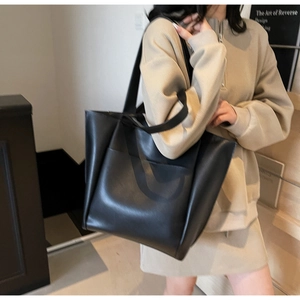 Detailed view of a black tote bag showing the fine leather texture and front pocket design