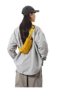 Adjustable yellow crossbody waist bag in nylon material worn by model over gray clothing