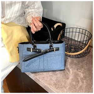 Detail of light blue denim handbag with black leather straps and buckle on stone table