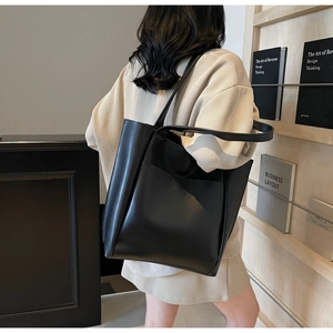 Minimalist black leather tote bag with open pocket shown on shoulder in office setting
