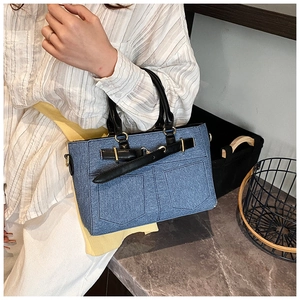 Detail of blue denim bucket bag with black leather handles and gold metal hardware accents