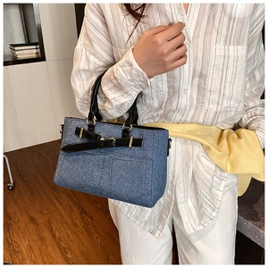 Close-up of blue denim texture tote bag with black leather straps and gold buckle