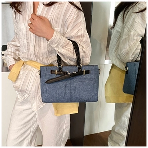 Close-up of blue denim bucket bag with black leather handles and gold metal hardware