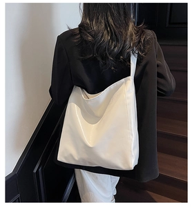 Glossy white PU leather tote bag with wide strap on shoulder of a model in black suit