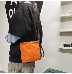 Close-up of bright orange nylon crossbody bag with textured fabric and black strap