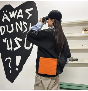 Close-up of vibrant orange nylon crossbody bag worn by a model in a trendy urban setting