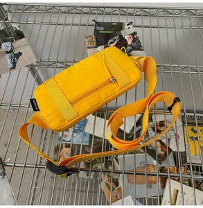 Detail view of bright yellow nylon crossbody bag with layered zippers on a grid shelf