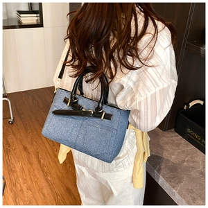 Close-up of blue denim bucket bag with black leather handle and gold hardware on model