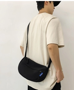 Close-up of black minimalist crossbody bag with adjustable strap and blue woven logo