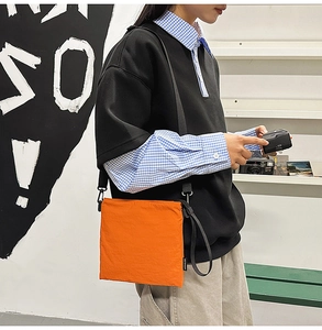 Detail of trendy orange nylon square crossbody bag with adjustable strap on fashion model