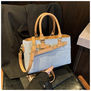 Close-up of light blue denim bucket bag with brown leather handles and gold hardware