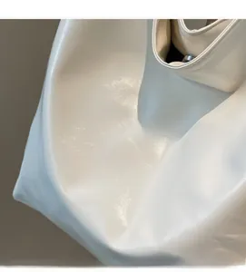 Detail of soft white leather tote bag featuring a polished texture and silver magnetic clasp