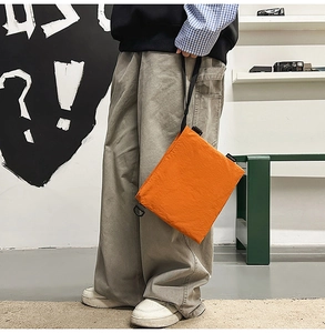 Close-up of bright orange utility crossbody bag with black cord on street background