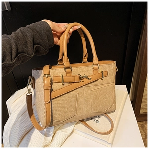 Detail of a beige canvas bucket bag with brown leather trim and metal buckle straps
