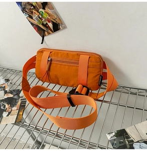 Detail of vibrant orange nylon crossbody bag featuring heavy-duty buckles and zip pockets