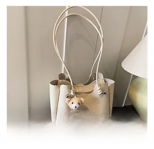 Detail of cream-white lychee grain leather bucket bag featuring a cute teddy bear charm