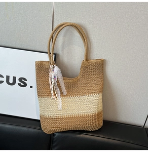 Detail of two-tone woven straw tote bag with decorative white lace tassel charm