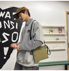 Detail of grey polo shirt with ManyStory logo, green canvas bag and yellow cap outfit