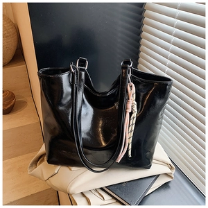 Detail of glossy black tote bag featuring woven tassel charm and textured faux leather finish