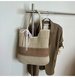 Detail of straw woven tote bag with white lace bow and colorful bead charm hanging on a rack