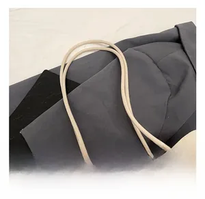 Detail of beige litchi grain leather bucket bag with minimalist knotted rope handle