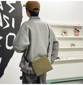 Rear view of an olive green canvas crossbody bag on a model wearing casual streetwear