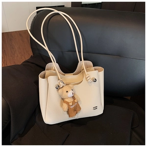 Close-up of cream lychee texture tote bag with a cute teddy bear plush charm and brand logo