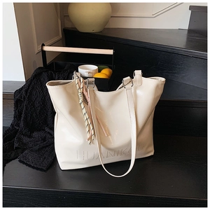 Detail of cream tote bag featuring embossed logo and striped decorative cord on steps