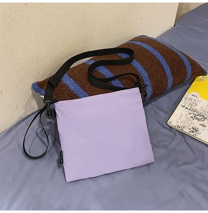 Detailed view of lilac nylon envelope bag with black strap on casual bedding scene