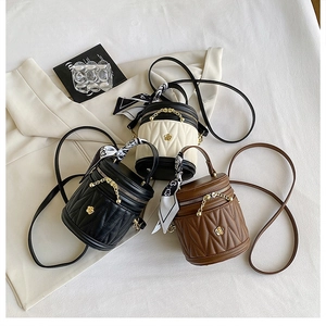 Close-up of quilted bucket bags in black, beige, and brown with gold flower logo details