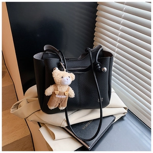 Detail of black lychee texture tote bag with a cute teddy bear charm on casual books