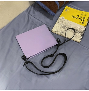 Detail of light purple nylon phone bag with adjustable black strap and logo tag