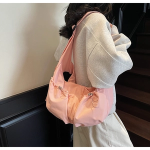 Détail du sac bandoulière rose en nylon plissé porté par un mannequin sur un escalier