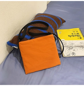 Close-up of bright orange nylon envelope crossbody bag with adjustable black shoulder strap