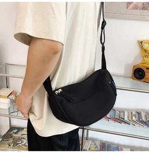 Side view of a black crescent nylon crossbody bag worn by a person in a casual home setting