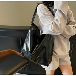 Detail view of a black glossy tote bag with wide strap on a model for daily commute style