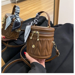 Close-up of quilted brown bucket bag with floral logo and silk scarf handle detail