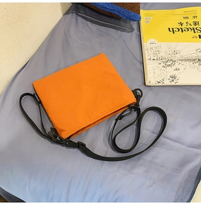 Detail of bright orange nylon crossbody bag with adjustable strap on light blue background