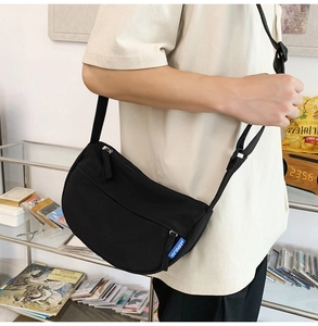 Detail view of a black nylon crescent crossbody bag with adjustable strap on a model