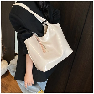 Close-up of creamy beige glossy tote bag with stylish tassel detail on model shoulder