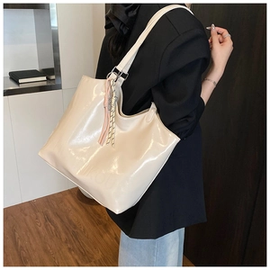Detail of cream glossy tote bag with woven charm and embossed logo on model's shoulder