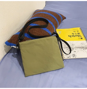 Detail of green nylon envelope bag with adjustable black strap on a cozy bedding setup