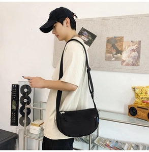 Side view of black nylon crescent crossbody bag worn by a model in a minimalist setting